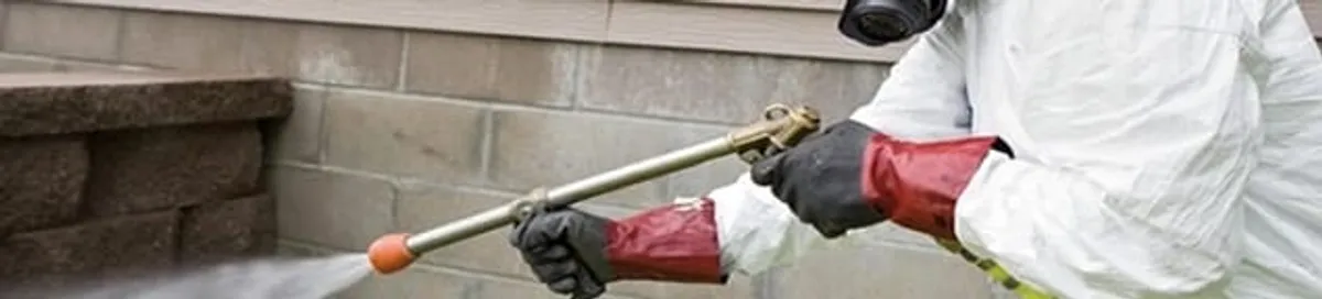 Pest control technician applying exterior insect treatment along a home foundation in Jersey City, NJ
