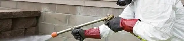 Pest control technician applying exterior insect treatment along a home foundation in Jersey City, NJ