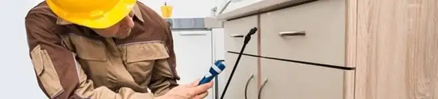 Roach exterminator applying treatment under kitchen cabinets in Jersey City, NJ