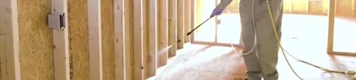 Termite treatment technician applying spray along framing and unfinished walls in Jersey City, NJ