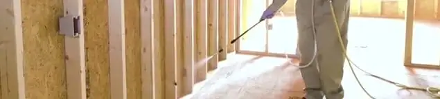 Termite treatment technician applying spray along framing and unfinished walls in Jersey City, NJ